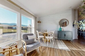 A room with a large window, a dining table, chairs, a sofa, a small table, and a cabinet.