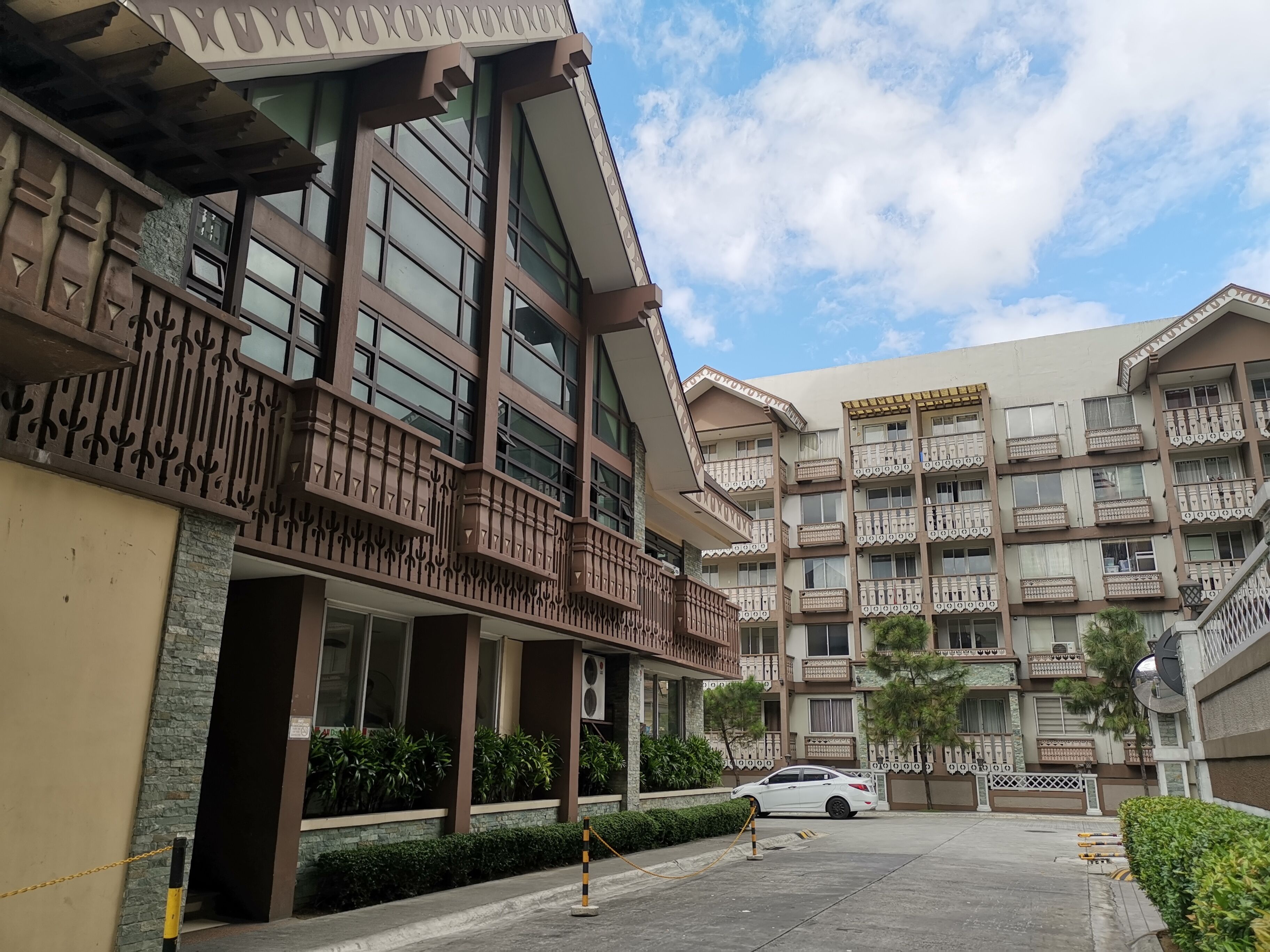 A multi-story residential building with balconies, a gated entrance, and a parked car.