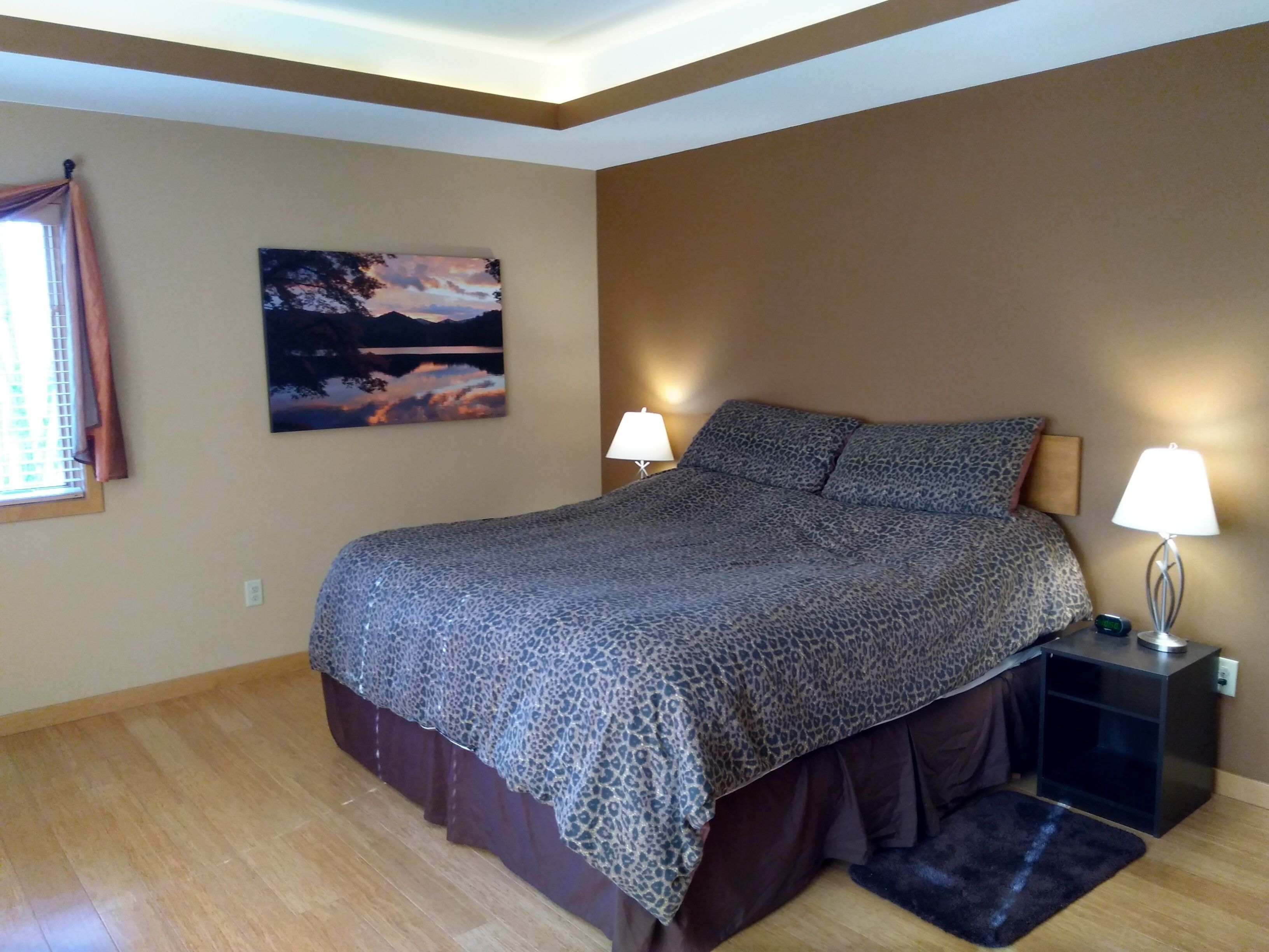 Un dormitorio con una cama, dos lámparas de noche, una mesita de noche, una alfombra y un cuadro en la pared.