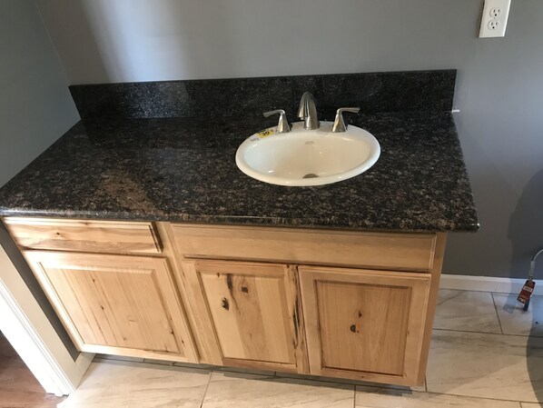 Ein Badezimmer mit einer Granitplatte, einem weißen Waschbecken und Holzschränken.