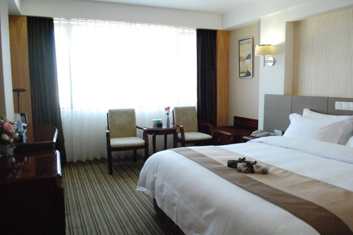 Une chambre d’hôtel avec un grand lit, deux fauteuils, une petite table, un bureau et une lampe.