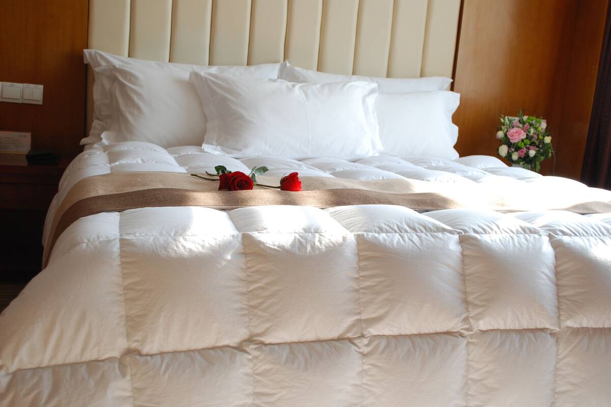 Un lit bien fait, avec du linge de lit blanc et deux roses rouges.