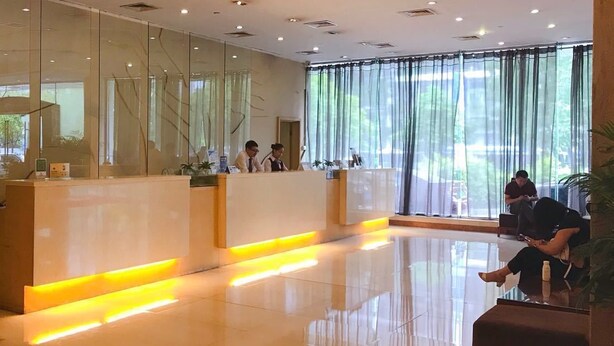 A modern reception area with a glass partition, a reception desk, and a seating area with a plant. - Shenzhen Sichuan Hotel (Shenzhen)