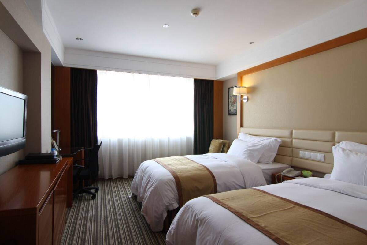 Une chambre d’hôtel avec deux lits, un bureau, une chaise, une télévision et une fenêtre avec des rideaux.