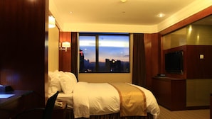 A hotel room with a bed, a desk, a chair, a TV, and a large window with a city view. - Shenzhen Sichuan Hotel (Shenzhen)