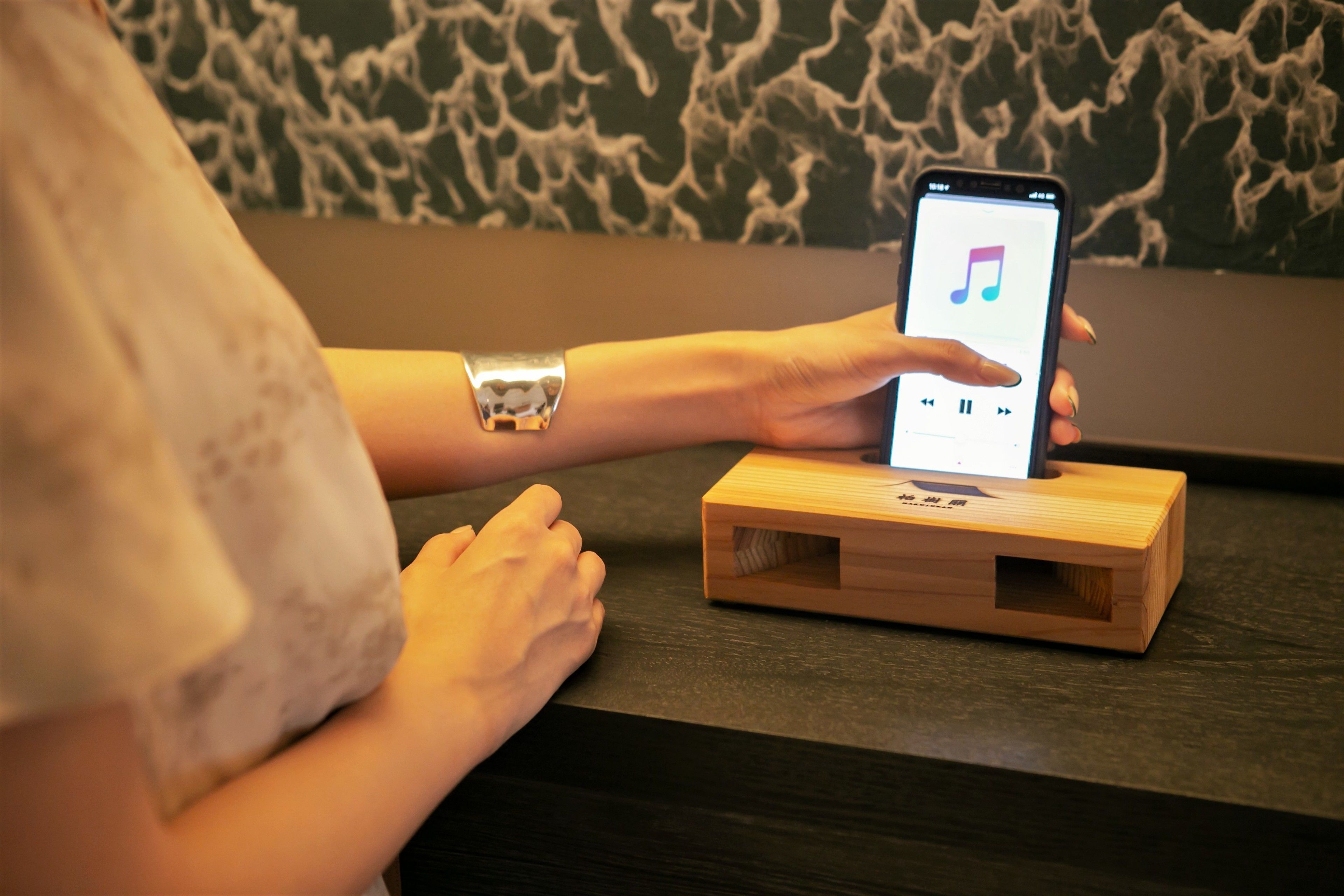 A person holding a smartphone with a music app interface, resting on a wooden stand.