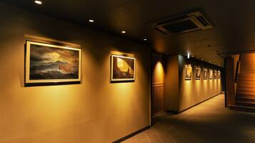 A hallway with framed artwork on the walls, a wooden staircase, and recessed lighting.