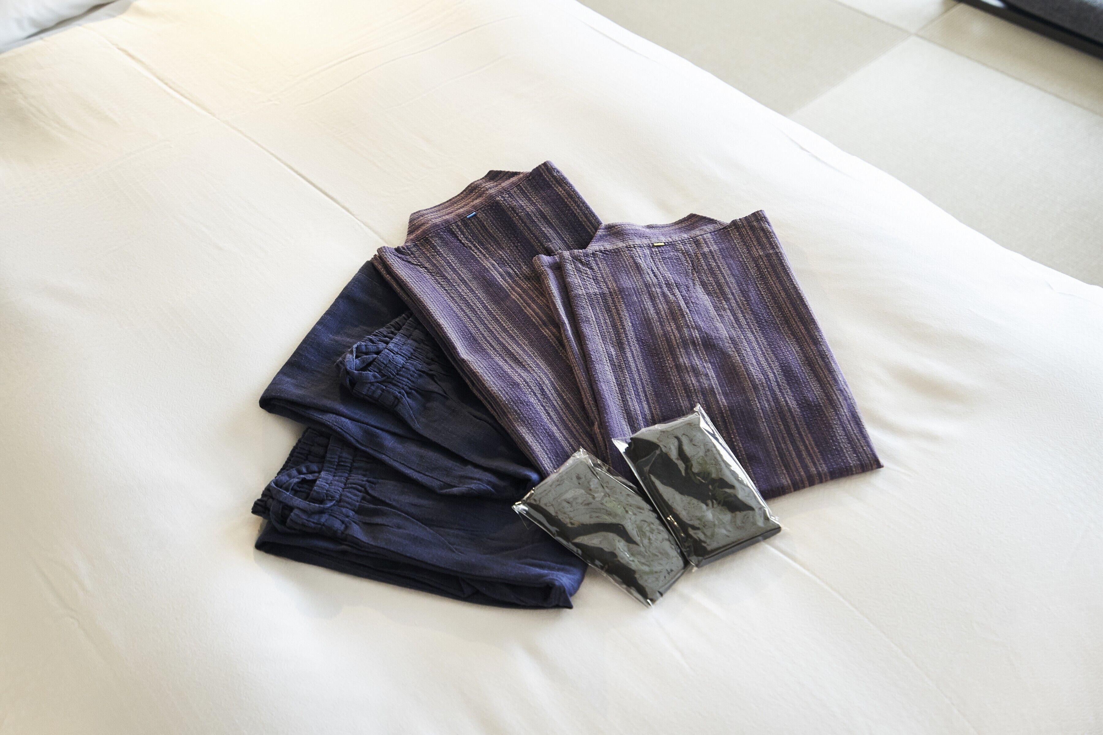 A neatly arranged bed with folded clothes and a small bag on it.