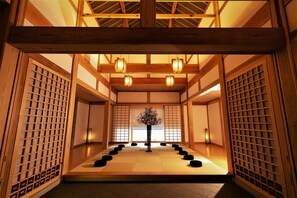 Una habitación japonesa tradicional con suelo de tatami, puertas correderas de madera y un árbol decorativo en el centro.