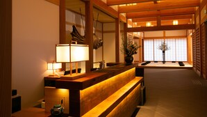 Un espace d’accueil avec un comptoir en bois, une lampe, un vase de fleurs et, au fond, une porte coulissante de style japonais traditionnel.