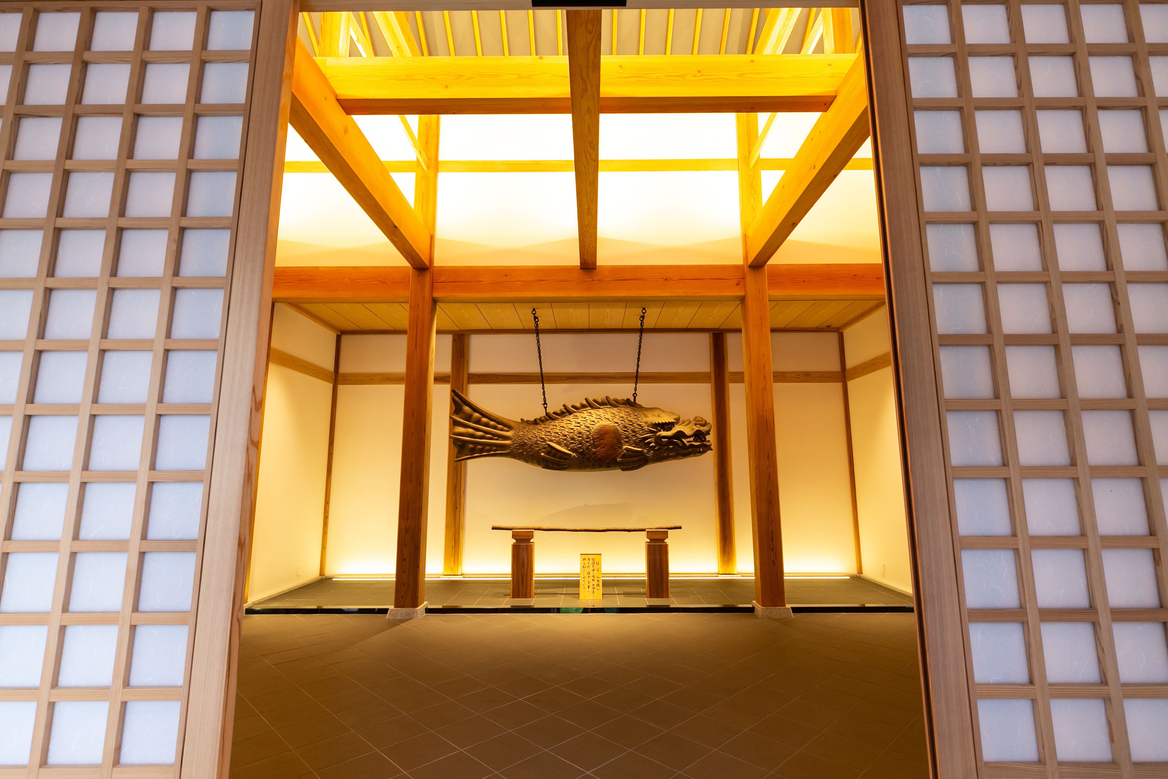 Una tradizionale stanza giapponese con pavimento in tatami, soffitto con travi di legno e una scultura a forma di pesce appesa.
