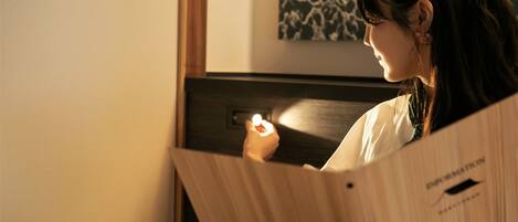 A person sitting at a wooden table with a laptop, in a room with a wooden headboard and a wall-mounted artwork.