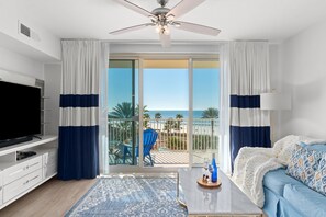 Un soggiorno moderno con televisione a schermo piatto, tavolino da caffè e divano. Sul balcone, vista sulla spiaggia e palme.