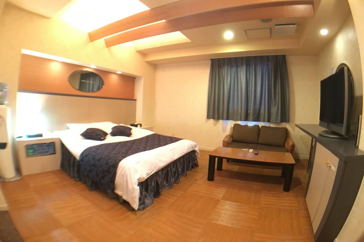 A hotel room with a bed, a desk, a television, and a window with curtains.