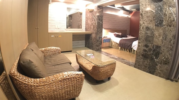 A room with a woven sofa, a glass coffee table, and a bed with a headboard. - Hotel Orchidee - Adult Only (Kurashiki)
