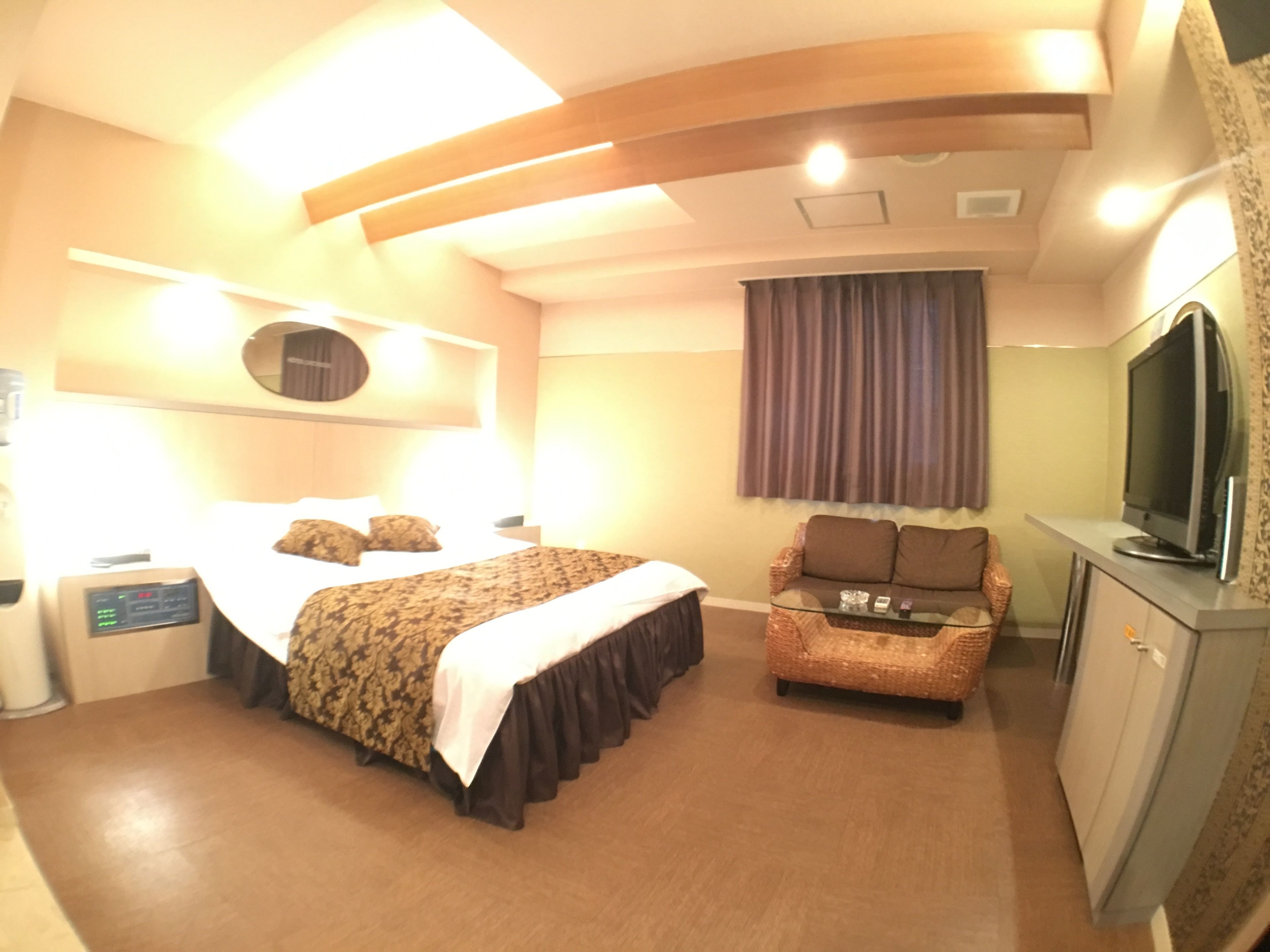 Habitación de hotel con cama, una silla, un escritorio con televisor y un espejo en la pared.