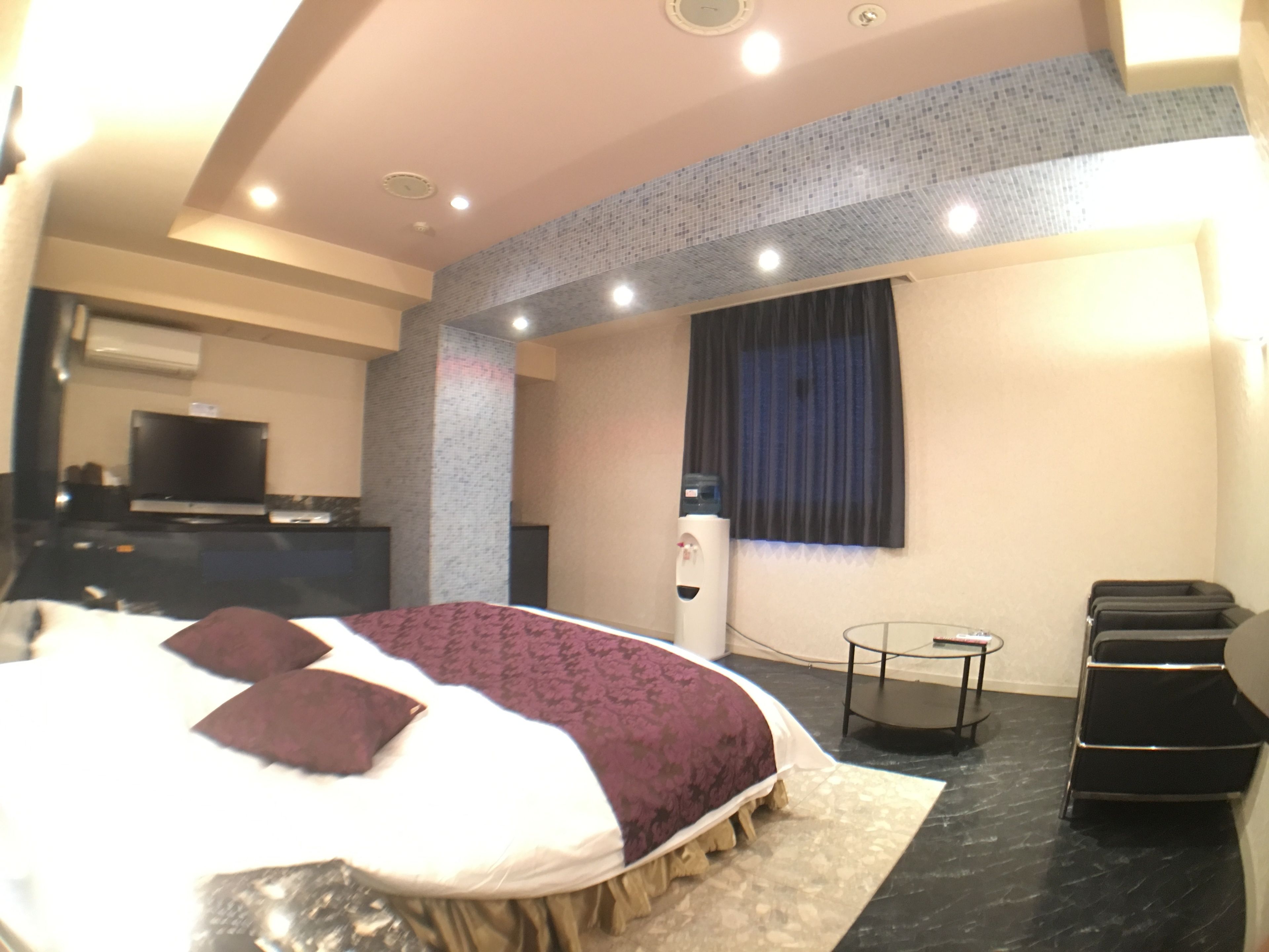 Une chambre d’hôtel moderne équipée d’un grand lit, d’une petite table, d’une télévision et d’un distributeur d’eau.