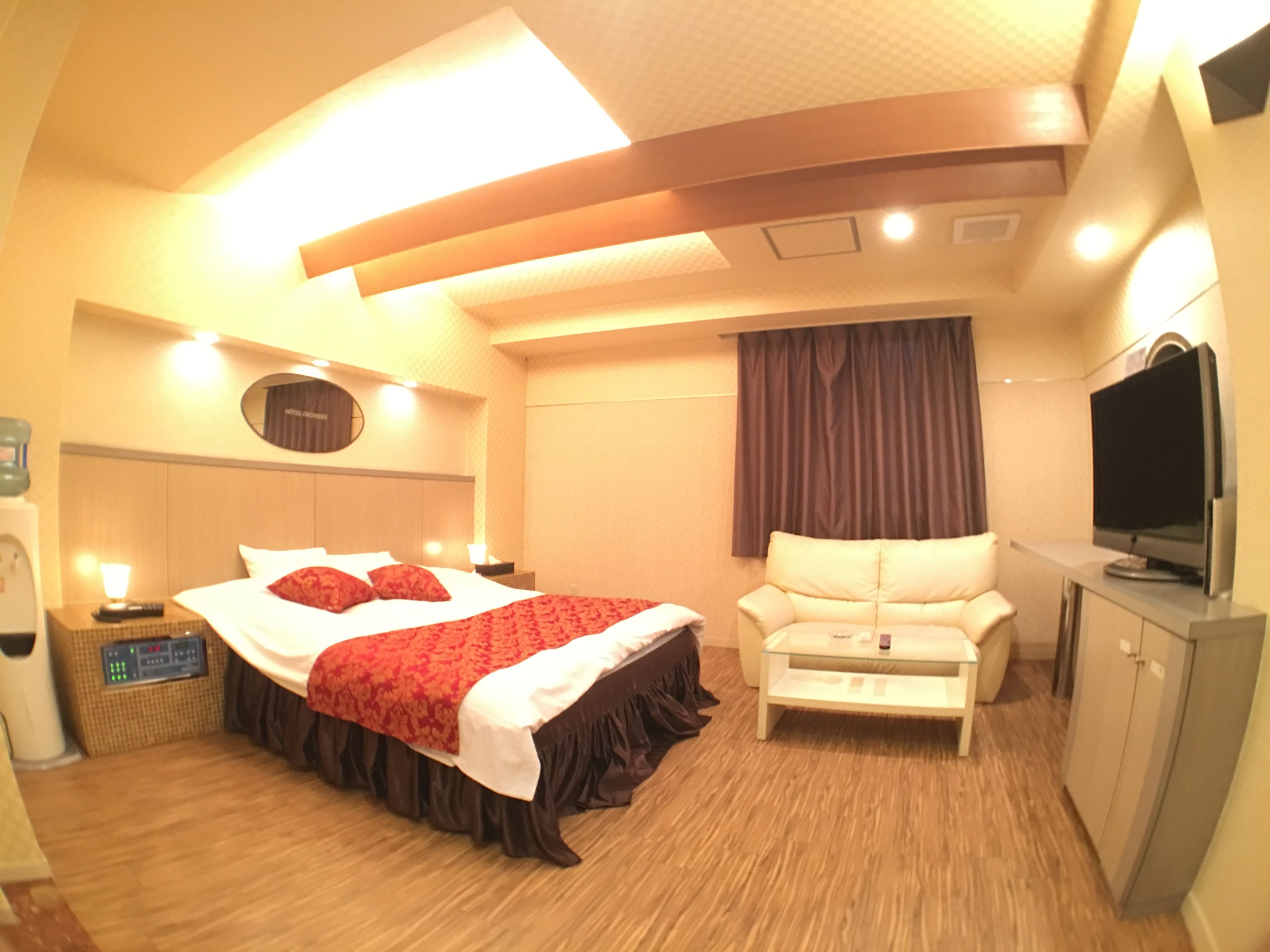 A hotel room with a bed, a sofa, a television, and a minibar.