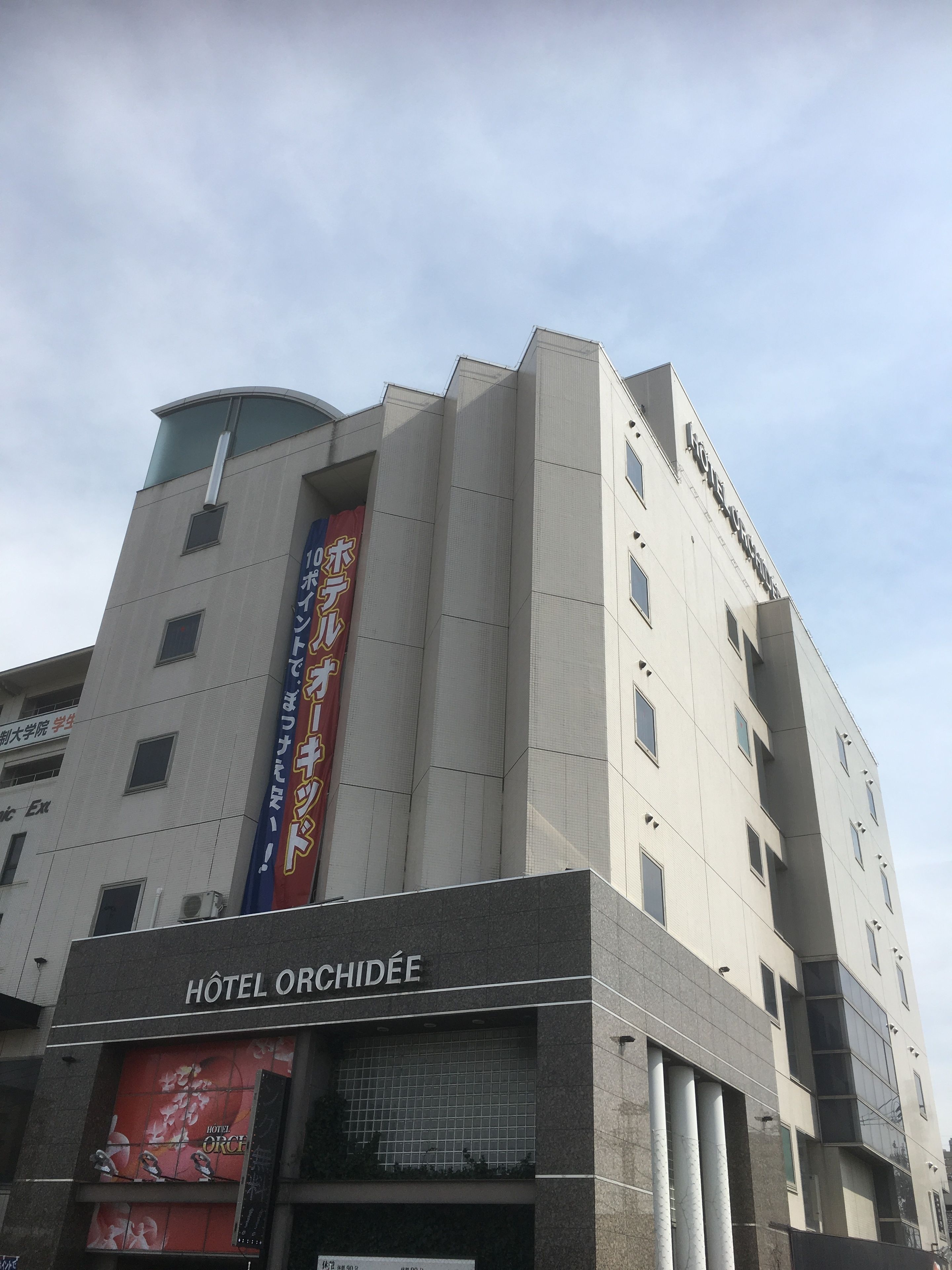 Un hotel de diseño moderno, con un llamativo cartel vertical con texto japonés y un letrero que dice "HOTEL ORCHIDÉE" en la parte inferior.