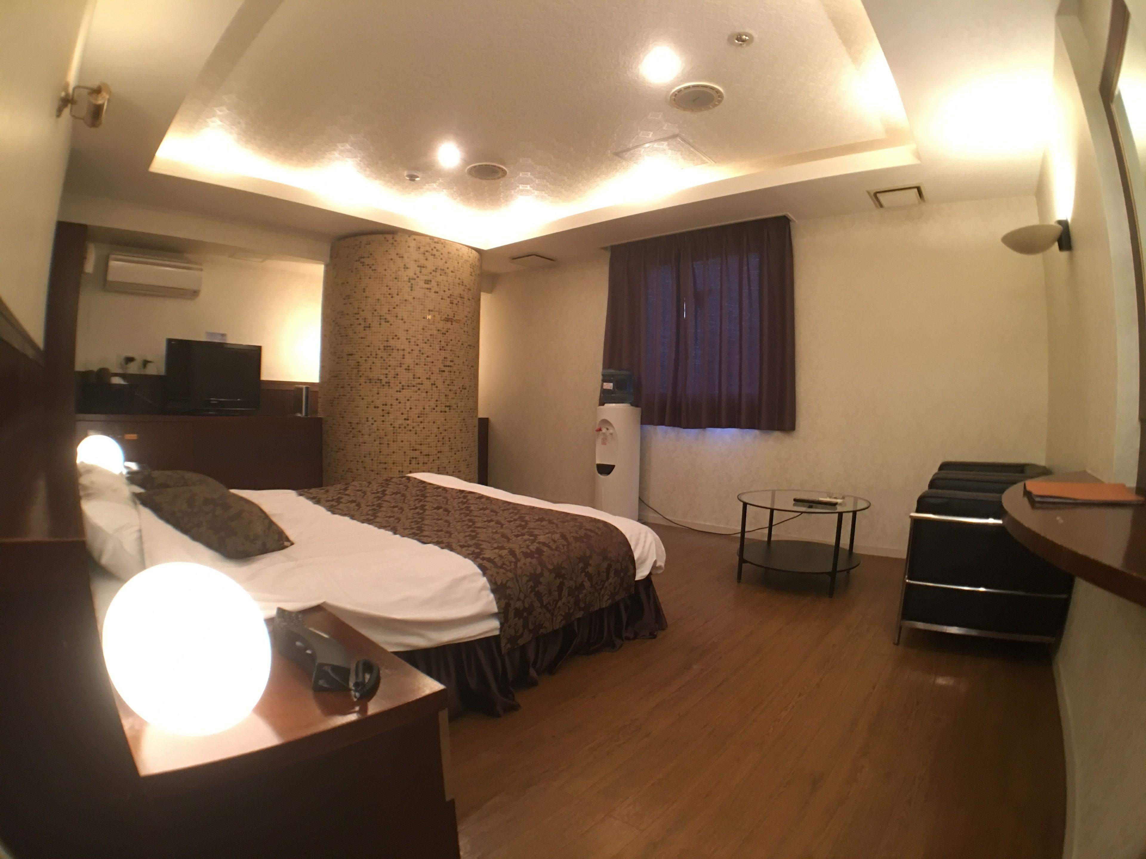 Une chambre d’hôtel équipée d’un lit, d’une table de chevet, d’une lampe, d’un distributeur d’eau et d’une petite table avec une télécommande.