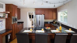Une cuisine moderne dotée de meubles en bois, d’appareils électroménagers en acier inoxydable, d’un îlot central avec des sièges et d’une fenêtre qui laisse entrer la lumière naturelle.