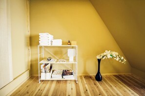 Un rincón de habitación con suelo de madera, un estante blanco con toallas dobladas, un jarrón con flores y una pared de madera.