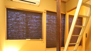 Una habitación con pisos de madera, alfombra gris y aire acondicionado blanco, además de una escalera de madera.