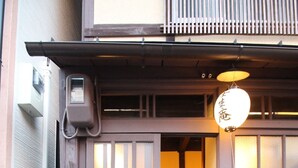 Una entrada tradicional japonesa con puerta corredera, un pequeño porche y un farol colgante.