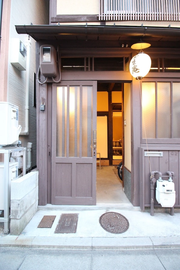 Una entrada tradicional japonesa con puerta corredera, un pequeño porche y un farol colgante.