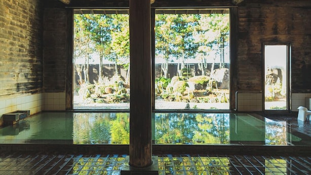 A traditional Japanese onsen with a view of a natural landscape through large windows.