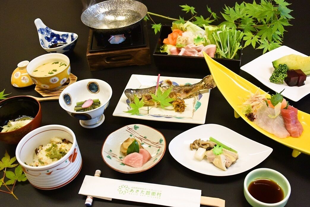 Diverse Japanse gerechten, waaronder sushi en sashimi, gepresenteerd op een tafel met traditionele theeserviezen en een theepot.