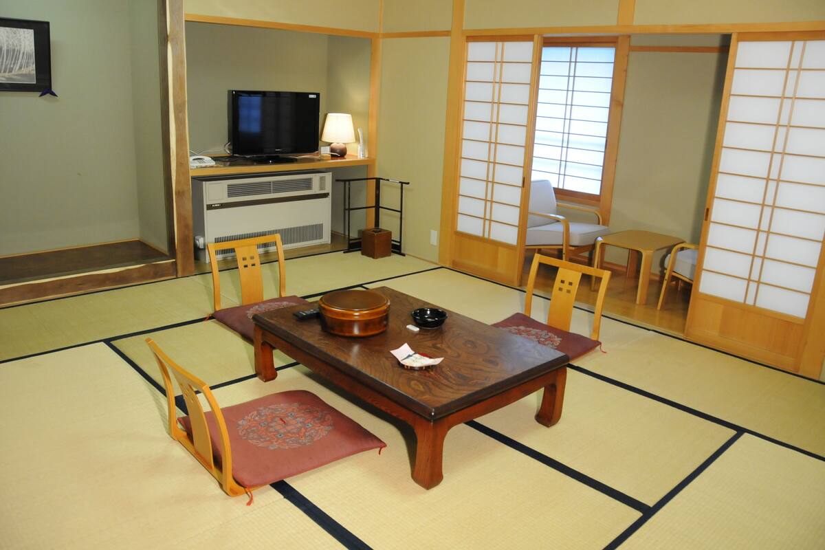 A traditional Japanese room with tatami flooring, a low table with a tea set, and sliding doors.
