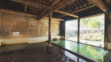 Um onsen japonês tradicional com interior em madeira, chão ladrilhado e vista para o exterior por grandes janelas.