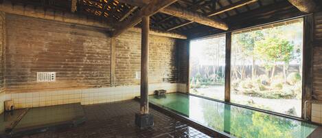 A traditional Japanese onsen with a wooden interior, a tiled floor, and a view of the outdoors through large windows.