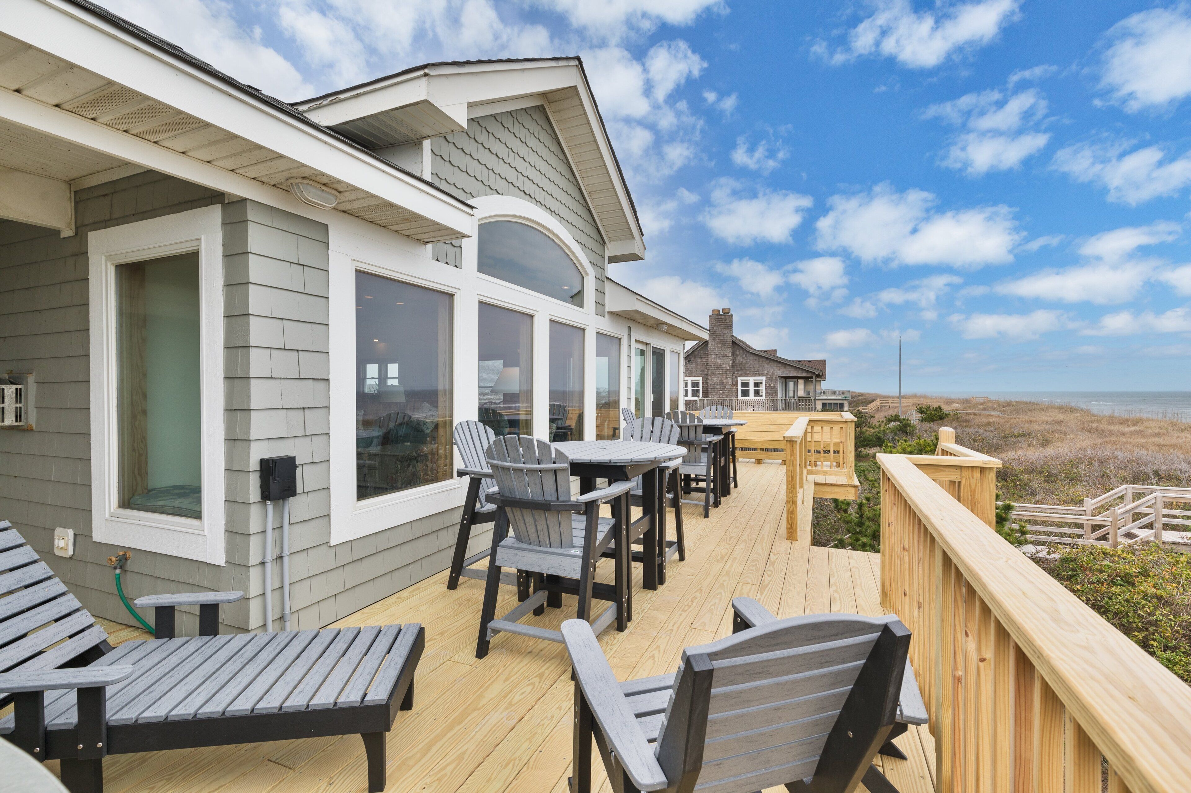A deck with outdoor seating and large windows overlooking the beach.