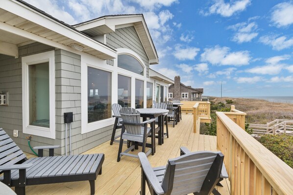 A deck with outdoor seating and large windows overlooking the beach. - 2440 - Solitude South - Oceanfront Duck Retreat | Sleeps 15 + Hot Tub (Duck)