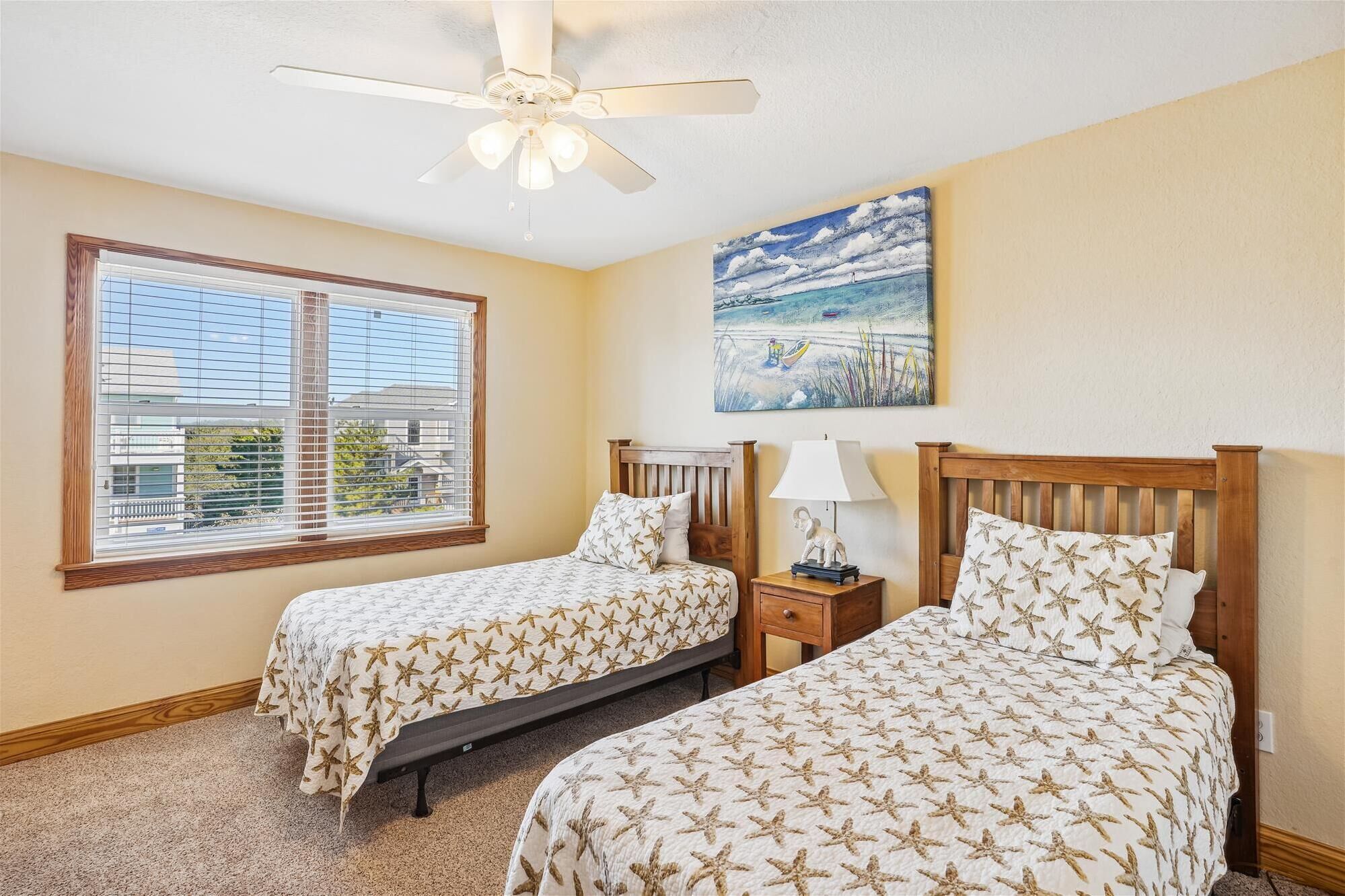 A bedroom with two beds, a ceiling fan, a painting, and a window with blinds.