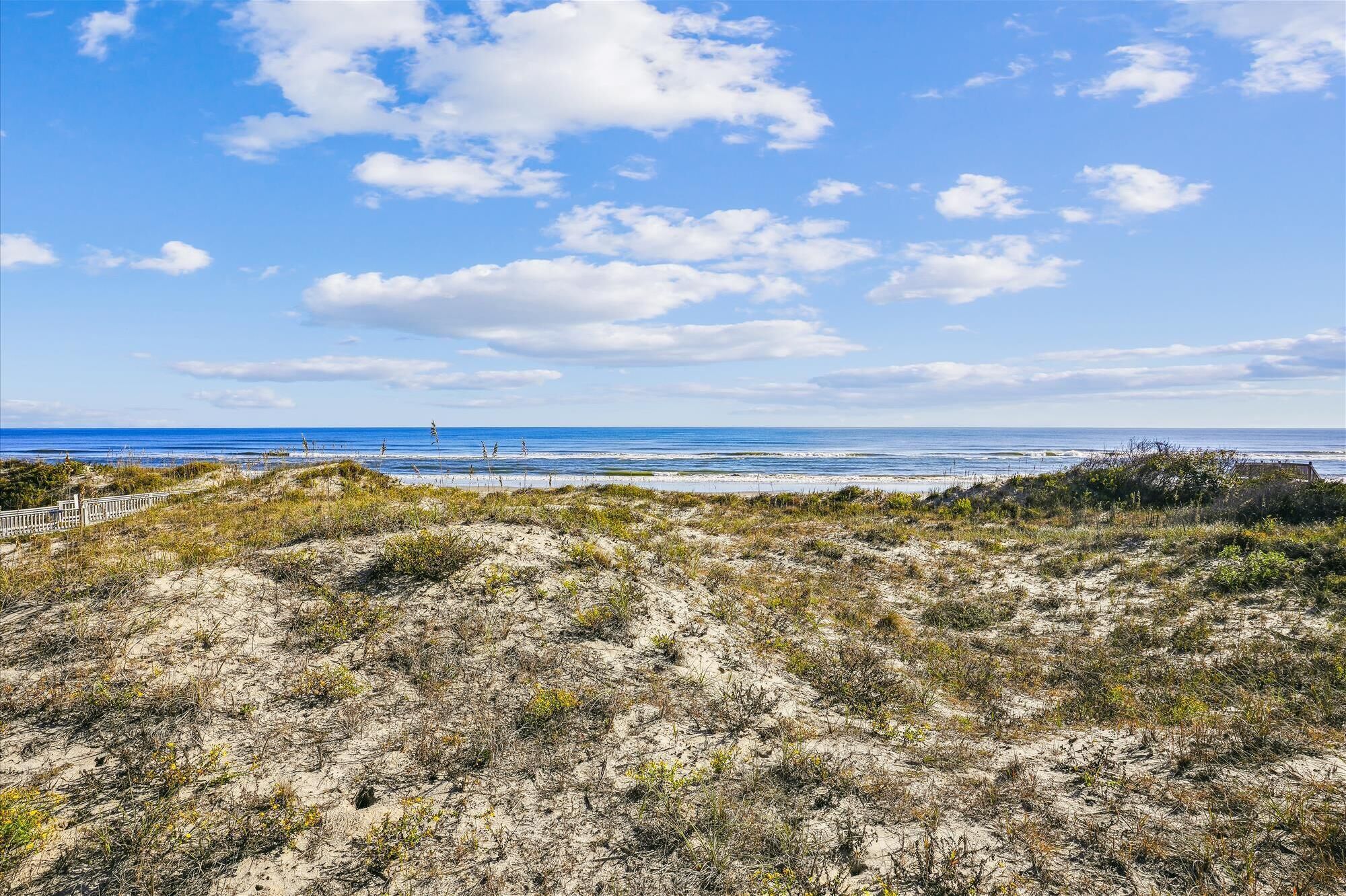 A coastal landscape with dunes, a beach, and a clear sky.