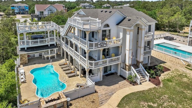 Une grande maison à plusieurs étages, dotée d’une piscine, de plusieurs terrasses et d’un patio couvert.