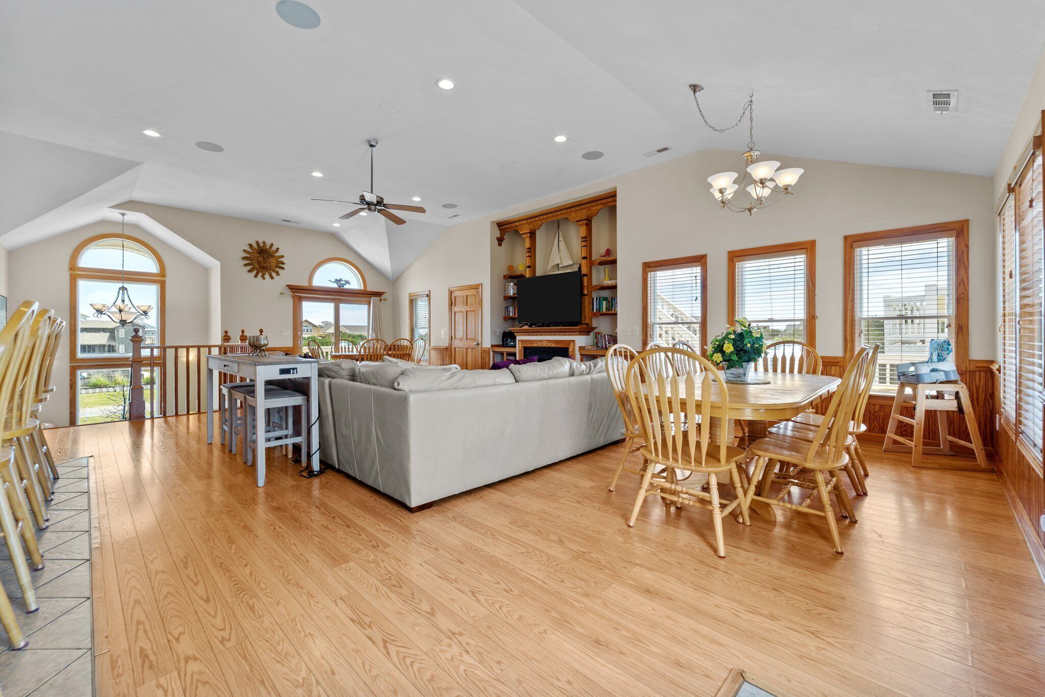 A spacious living area with a large sofa, dining table, and chairs, a television, and a ceiling fan.