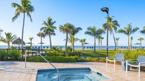 A pool area with a clear view of the ocean, surrounded by palm trees and lounge chairs. - Gulf-View & Fully Renovated Condo E31— Steps to the Beach at Pointe Santo (Sanibel)