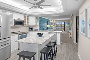 A modern kitchen with white cabinetry, a marble island, and a ceiling fan. - Gulf-View & Fully Renovated Condo E31— Steps to the Beach at Pointe Santo (Sanibel)