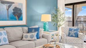 A living room with a sofa, armchair, and a coffee table with a tray. There is a lamp and a plant on a side table. - Gulf-View & Fully Renovated Condo E31— Steps to the Beach at Pointe Santo (Sanibel)