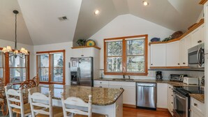 A kitchen with a central island, wooden chairs, a refrigerator, a dishwasher, and a microwave. - 1289 - Sounds Like Fun, Soundfront Corolla | Pool, Hot Tub & Resort Access (Corolla)