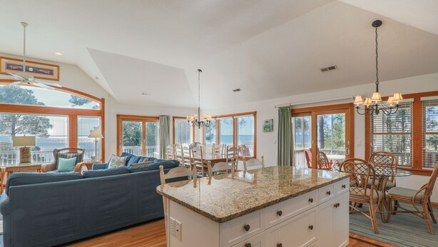 A spacious living area with a large island, wooden flooring, and a view of the outdoors through large windows. - 1289 - Sounds Like Fun, Soundfront Corolla | Pool, Hot Tub & Resort Access (Corolla)