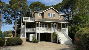 A two-story house with a balcony, a covered porch, and a staircase leading to the entrance. - 1289 - Sounds Like Fun, Soundfront Corolla | Pool, Hot Tub & Resort Access (Corolla)
