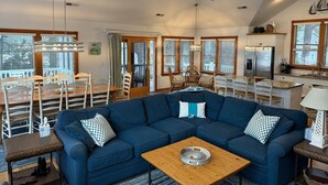 A spacious living area with a sectional sofa, dining table, and chairs. - 1289 - Sounds Like Fun, Soundfront Corolla | Pool, Hot Tub & Resort Access (Corolla)