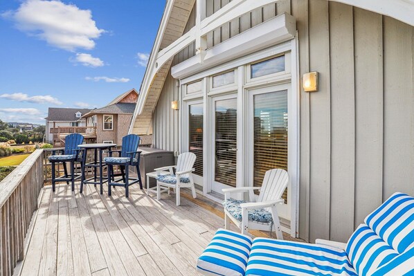A covered deck with outdoor furniture, including chairs and a sofa, and a view of the surrounding area.