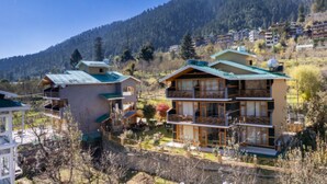 A multi-story building with balconies, surrounded by a mountainous landscape. - SNOW PEAK RETREAT & COTTAGES - MANALI (Centrally Heated) (Manali)