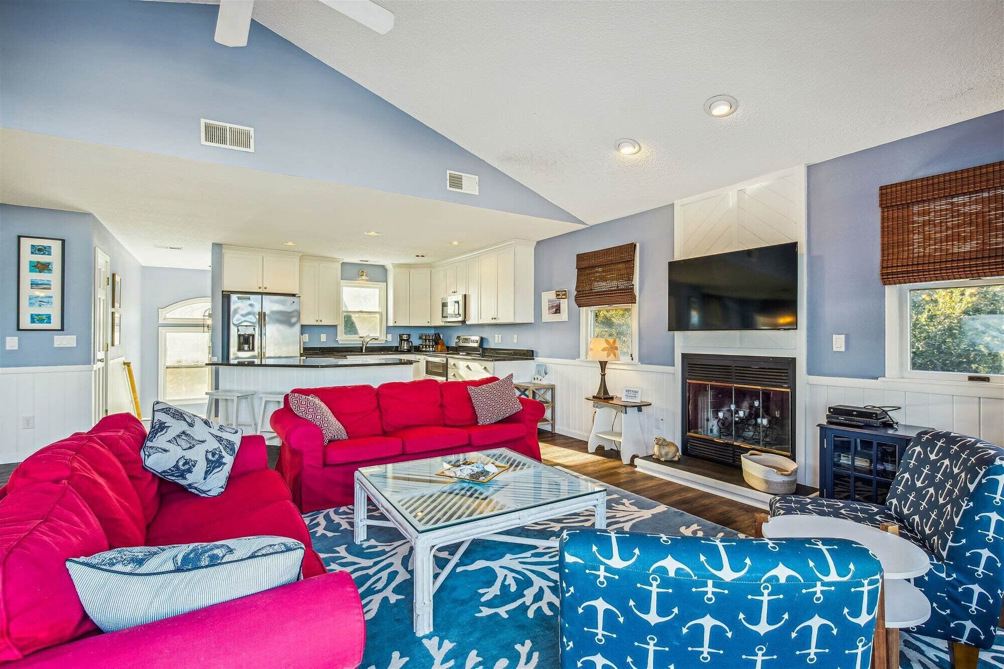 A living room with a red sofa, a blue patterned ottoman, and a glass coffee table.